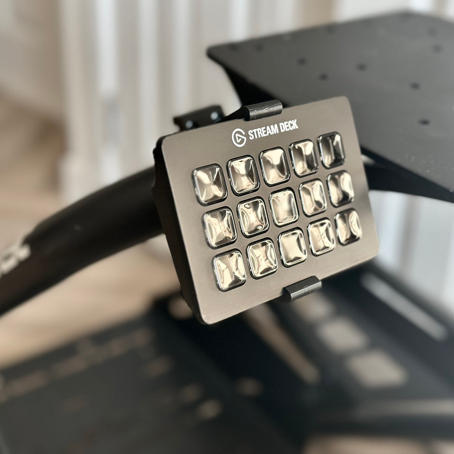 Playseat Trophy Stream Deck Mount installed on the tubular cockpit frame with a 15-key Stream Deck or Stream Deck Plus positioned beside the driving seat. The clamp attaches directly to the Playseat Trophy tube, while the RAM arm brings race controls into reach. This adjustable sim racing mount is available with a compact 5.5 cm arm or a longer 9.5 cm RAM arm for additional reach.