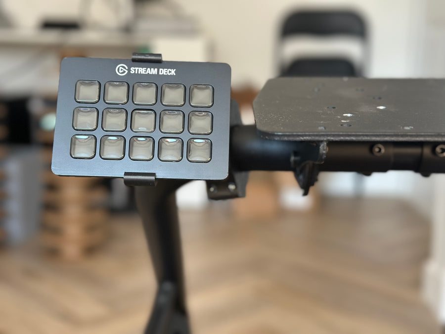 Playseat Trophy Stream Deck Mount installed on the tubular cockpit frame with a 15-key Stream Deck or Stream Deck Plus positioned beside the driving seat. The clamp attaches directly to the Playseat Trophy tube, while the RAM arm brings race controls into reach. This adjustable sim racing mount is available with a compact 5.5 cm arm or a longer 9.5 cm RAM arm for additional reach.