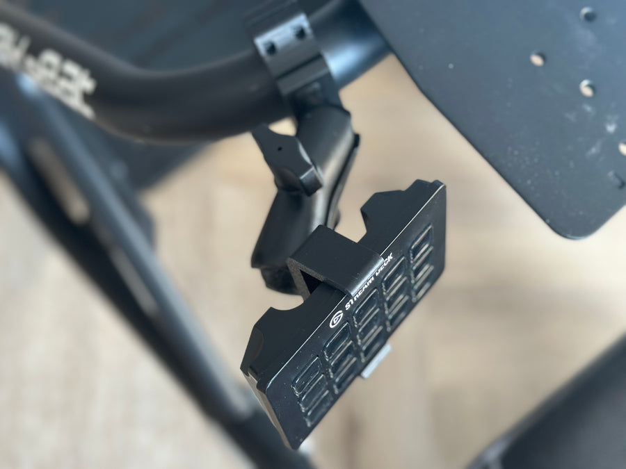 Playseat Trophy Stream Deck Mount installed on the tubular cockpit frame with a 15-key Stream Deck or Stream Deck Plus positioned beside the driving seat. The clamp attaches directly to the Playseat Trophy tube, while the RAM arm brings race controls into reach. This adjustable sim racing mount is available with a compact 5.5 cm arm or a longer 9.5 cm RAM arm for additional reach.