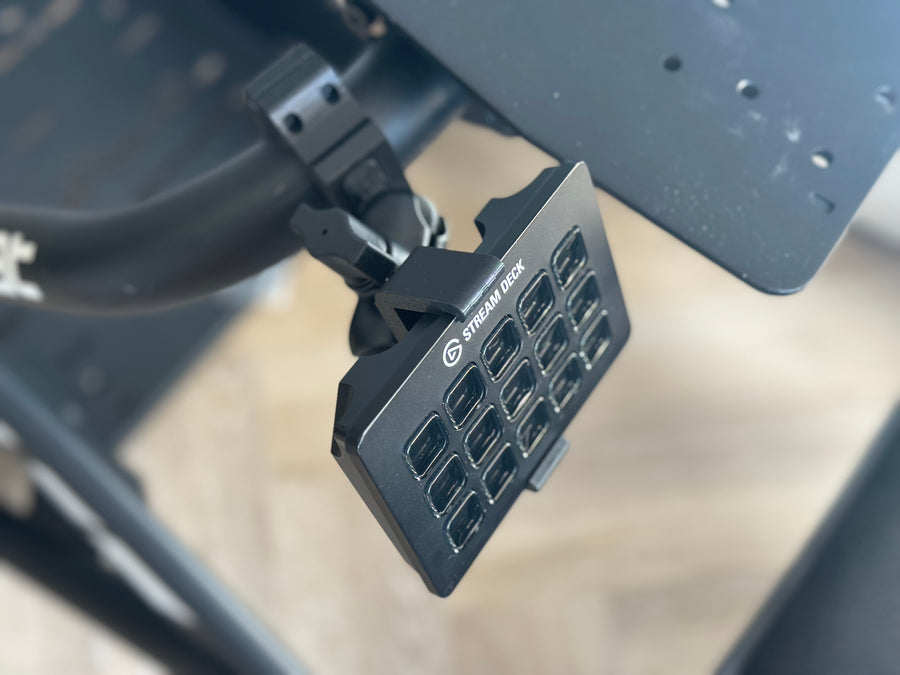 Playseat Trophy Stream Deck Mount installed on the tubular cockpit frame with a 15-key Stream Deck or Stream Deck Plus positioned beside the driving seat. The clamp attaches directly to the Playseat Trophy tube, while the RAM arm brings race controls into reach. This adjustable sim racing mount is available with a compact 5.5 cm arm or a longer 9.5 cm RAM arm for additional reach.